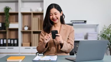 Genç ve güzel bir kadın iş yerinde otururken akıllı telefon ve dizüstü bilgisayar kullanıyor. Modern ofiste işe odaklanmış. 