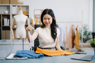 Asyalı terzi kadın terzi atölyesinde giysiler üzerinde çalışıyor. Modern stüdyoda başarılı olduktan sonra güzel genç bayan moda tasarımcısı gülümsemesi