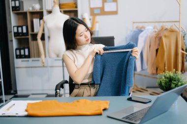 Asyalı terzi kadın terzi atölyesinde giysiler üzerinde çalışıyor. Modern stüdyoda başarılı olduktan sonra güzel genç bayan moda tasarımcısı gülümsemesi