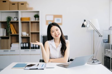 Modern ofiste gülümseyen ve dizüstü bilgisayar kullanan çekici Asyalı kadın ofis çalışanı.