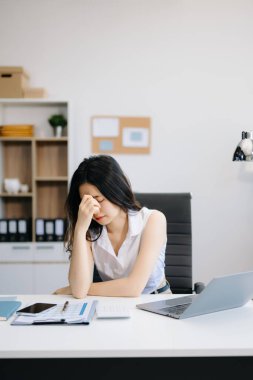 Asyalı kadın migren ağrısı çekiyor. Ofiste dizüstü bilgisayarla çalışırken çok çalışan iş kadını finansörü.