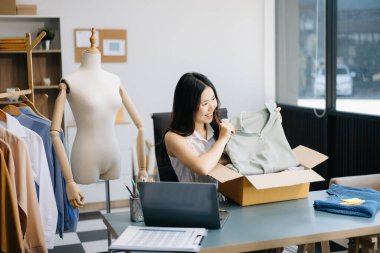 Güzel Asyalı bayan blogcu dükkanında canlı yayın yapan video kaydına kıyafetlerini kameranın önünde gösteriyor. Çevrimiçi Alışveriş Arabası kavramı