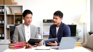 Asyalı iş adamları ve avukatlar masada dizüstü bilgisayarla kontrat belgelerini tartışıyorlar. Hukuk kavramları, tavsiyeler, hukuk hizmetleri. Ofiste