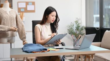  Moda tasarımcısının masasında dizüstü bilgisayar kullanan Asyalı genç bir kadın. 