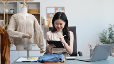  Moda tasarımcısının masasındaki Asyalı genç kadın stüdyodaki tablet bilgisayarda çalışıyor.