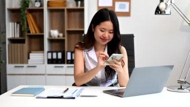 Ofiste çalışmak için akıllı telefon ve dizüstü bilgisayar kullanan çekici bir iş kadını.  