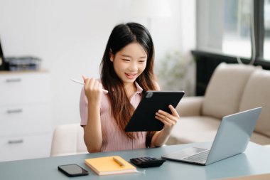 Ofiste dijital tablet ve dizüstü bilgisayar kullanan Asyalı kadın.