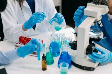 Bir tıp laboratuvarında araştırma yapan takım bilim adamları, ön plandaki bir araştırmacı, tıp laboratuarında bir mikroskop kullanıyor.. 