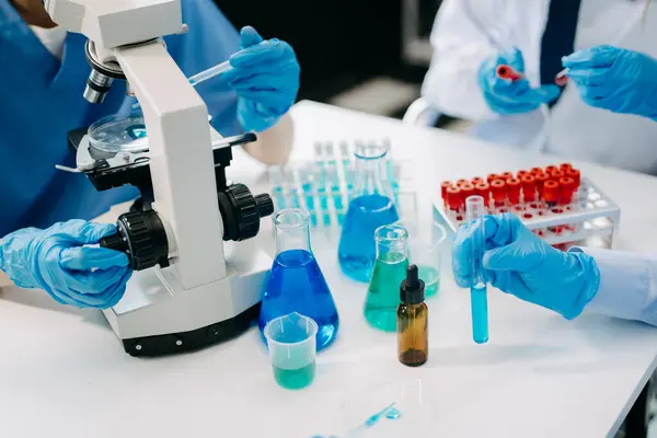 stock image Team scientists conducting research investigations in a medical laboratory, a researcher in the foreground is using a microscope in laboratory for medicine. 