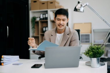 Yönetici yönetici dizüstü bilgisayar kullanıyor ve ofisteki deftere notlar yazıyor.