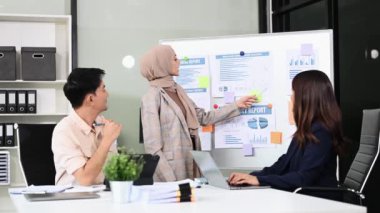 Bir grup genç Asyalı iş adamı bilgisayar ve dijital tablet kullanarak yaratıcı ofiste modern girişimin iş planını tartışıyor. 