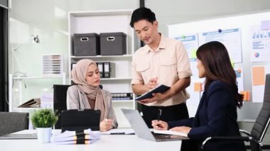 Bir grup genç Asyalı iş adamı bilgisayar ve dijital tablet kullanarak yaratıcı ofiste modern girişimin iş planını tartışıyor. 