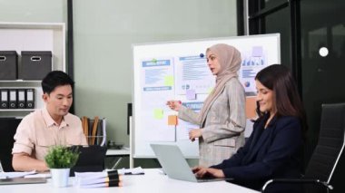 Bir grup genç Asyalı iş adamı bilgisayar ve dijital tablet kullanarak yaratıcı ofiste modern girişimin iş planını tartışıyor. 