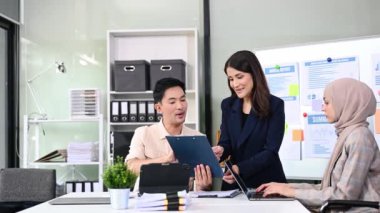 Bir grup genç Asyalı iş adamı bilgisayar ve dijital tablet kullanarak yaratıcı ofiste modern girişimin iş planını tartışıyor. 