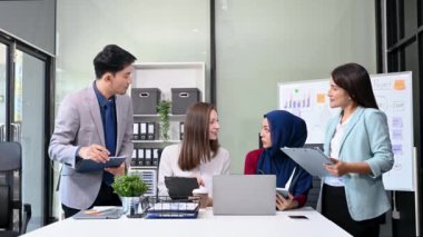 Bir grup genç Asyalı iş adamı bilgisayar ve dijital tablet kullanarak yaratıcı ofiste modern girişimin iş planını tartışıyor. 