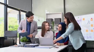 Bir grup genç Asyalı iş adamı bilgisayar ve dijital tablet kullanarak yaratıcı ofiste modern girişimin iş planını tartışıyor. 