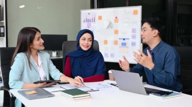 Bir grup genç Asyalı iş adamı bilgisayar ve dijital tablet kullanarak yaratıcı ofiste modern girişimin iş planını tartışıyor. 