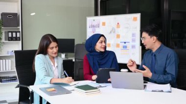 Bir grup genç Asyalı iş adamı bilgisayar ve dijital tablet kullanarak yaratıcı ofiste modern girişimin iş planını tartışıyor. 