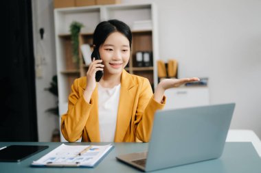 Başarılı Asyalı İş kadını Laptop 'ta Finans Analizi ve modern ofis masasında akıllı telefondan konuşma. vergi, rapor, muhasebe, istatistik ve analitik araştırma kavramı