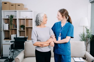 Genç hemşire yaşlı kadına odada yardım ediyor, destek oluyor. Destekli yaşam tesisinde yaralanma üstüne tedavi ve rehabilitasyon
