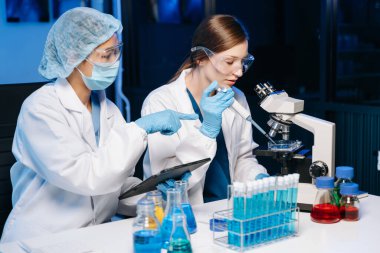 Tıp laboratuarında araştırma yapan genç bilim adamları, bir mikroskop ve tıp laboratuvarında dijital tablet kullanan araştırmacılar,.  