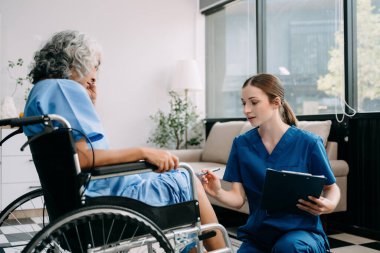 Genç hemşire yaşlı kadına yardım ediyor, elini tutuyor, destek oluyor. Destekli yaşam tesisinde yaralanma üstüne tedavi ve rehabilitasyon