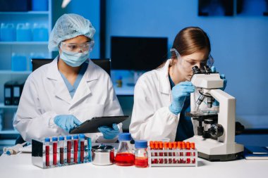 Tıp laboratuarında araştırma yapan genç bilim adamları, bir mikroskop ve tıp laboratuvarında dijital tablet kullanan araştırmacılar,.  