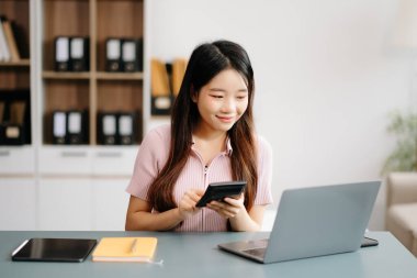 Ofiste akıllı telefon ve dizüstü bilgisayar kullanan Asyalı bir kadın.