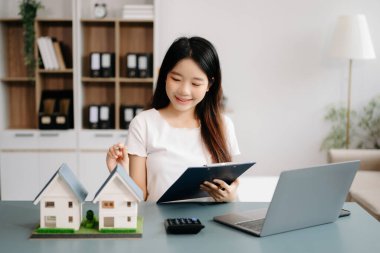 Modern ofiste dizüstü bilgisayarla çalışan genç bir emlakçı ve yanında küçük evler modeli.