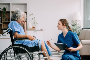 Genç hemşire, tekerlekli sandalyedeki yaşlı kadına yardım ediyor. Destekli yaşam tesisinde yaralanma üstüne tedavi ve rehabilitasyon
