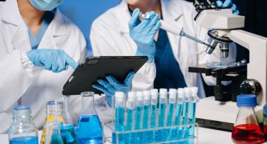 Tıp laboratuarında araştırma yapan genç bilim adamları, bir mikroskop ve tıp laboratuvarında dijital tablet kullanan araştırmacılar,.  