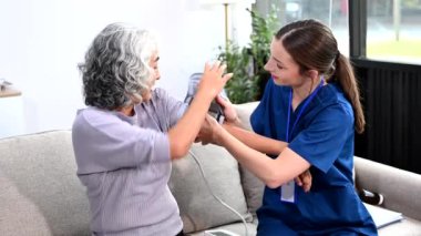 Genç hemşire yaşlı kadının tansiyonunu ölçmeye yardım ediyor. Destekli yaşam tesisinde yaralanma üstüne tedavi ve rehabilitasyon