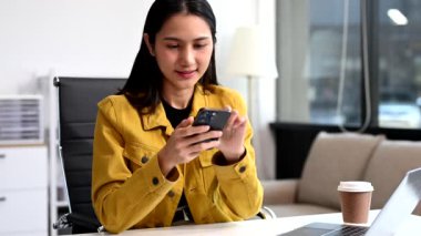 Ofiste çalışan Asyalı iş kadını akıllı telefon ve dizüstü bilgisayar kullanıyor. 