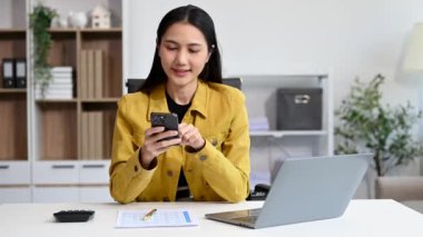 Ofiste çalışan Asyalı iş kadını akıllı telefon ve dizüstü bilgisayar kullanıyor. 