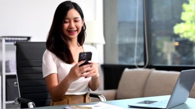 Ofiste çalışan Asyalı iş kadını akıllı telefon ve dizüstü bilgisayar kullanıyor. 