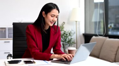 Asyalı İş kadını ofiste otururken dizüstü bilgisayar kullanıyor