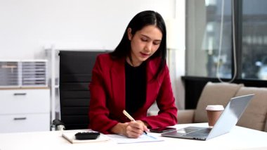 Asyalı İş kadını ofiste otururken dizüstü bilgisayar kullanıyor