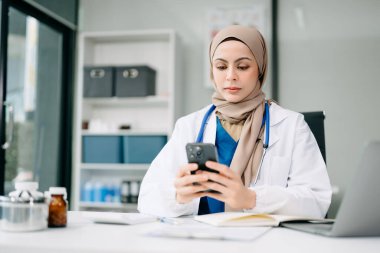 Ofis hastanesindeki masada oturan güzel doktor. İş için akıllı telefon ve dizüstü bilgisayar kullanan çekici kadın terapist. 