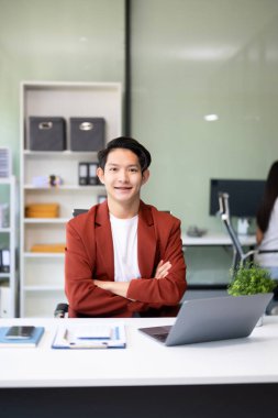 Ofisteki kameraya gülümseyen takım elbiseli yakışıklı Asyalı bir ofis çalışanı.