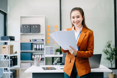 Young attractive Asian female office worker in business suit smiling at camera in modern office