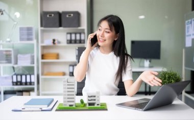 Emlak komisyoncusu ev modelini sunar. İş kadını, ofisteki ipotek kredisiyle ilgili akıllı telefondan müşteriye danışıyor 