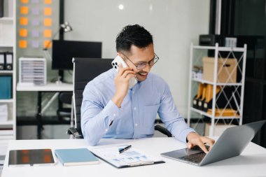 İş yerinde otururken Asyalı işadamı akıllı telefondan konuşuyor.