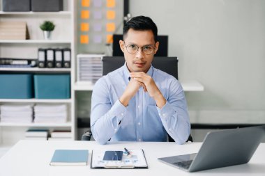 Asyalı işadamı ofiste oturuyor ve kameraya poz veriyor. 