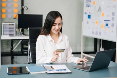 Asyalı kadın ödeme ve online alışveriş için kredi kartı ve dizüstü bilgisayar kullanıyor. 