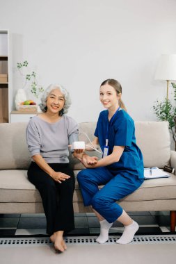 Doktor yaşlı hastayı tansiyon ölçer kullanarak muayene ediyor. Kanepede oturan yaşlı kadınla ilgilenen bir terapist. Tıbbi servis kavramı