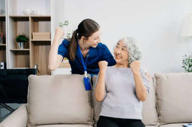 Hemşire ve yaşlı kadın hasta evde el kol hareketi yapıyor. Kanepede oturan yaşlı kadınla ilgilenen bir terapist. Tıbbi servis kavramı 