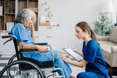 Hemşire evde yaşlı kadın hasta bacaklarına bakıyor. Tekerlekli sandalyede oturan yaşlı kadınla ilgilenen terapist. Tıbbi servis kavramı