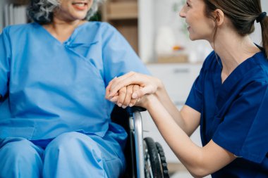 Nurse holding hands of older female patient at home. Therapist  taking care of senior woman sitting on wheelchair. Medical service concept