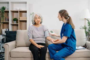 Doctor examining older patient using blood pressure gauge. Therapist at taking care of elderly woman sitting on sofa. Medical service concept