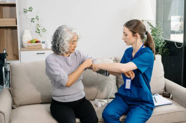 Doktor yaşlı hastayı tansiyon ölçer kullanarak muayene ediyor. Kanepede oturan yaşlı kadınla ilgilenen bir terapist. Tıbbi servis kavramı